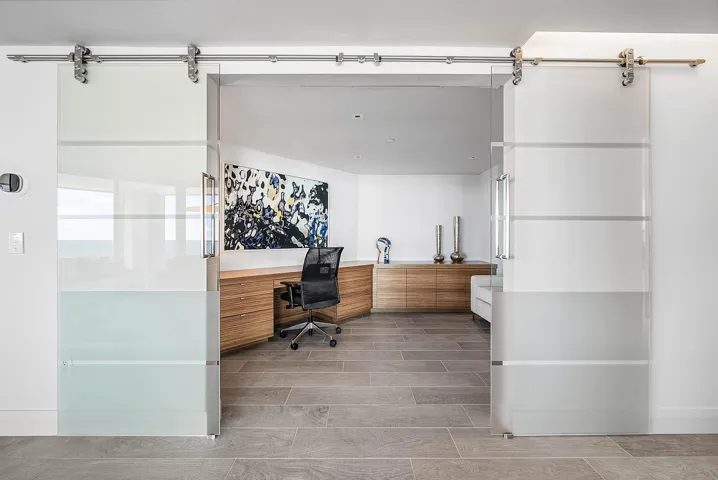 Dual frosted glass sliding doors with stainless steel hardware, wood-finish built-in cabinetry, recessed lighting, and large-format tile flooring
