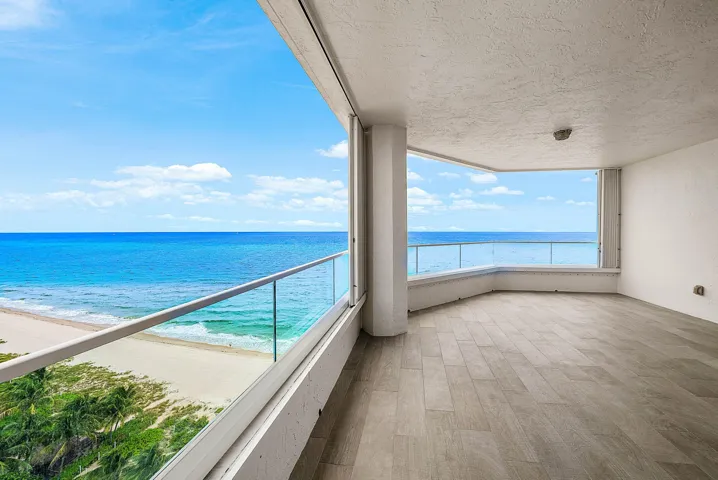 Covered balcony featuring wood-finish tile flooring, glass panel railings, and expansive ocean frontage