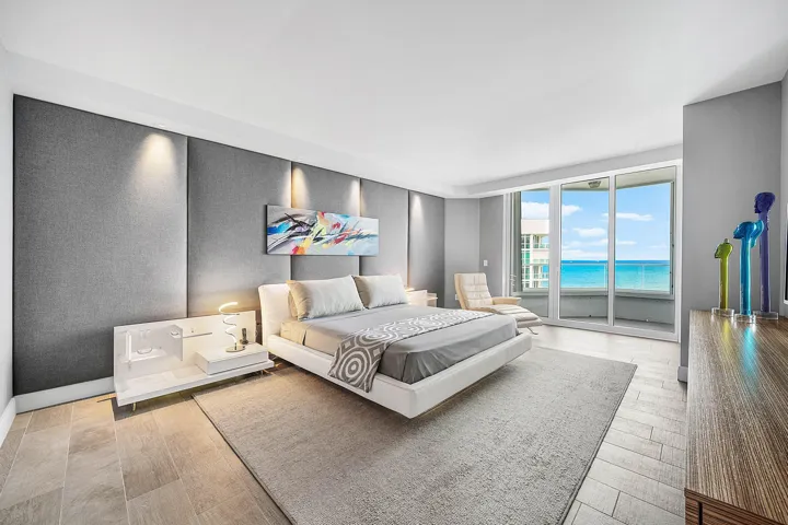 Full-height upholstered wall paneling with integrated accent lighting, tile flooring, and floor-to-ceiling glass sliding doors opening to an ocean backdrop