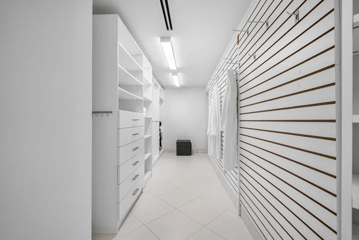 Walk-in closet featuring white built-in cabinetry with integrated drawers, slat-wall organizational system with adjustable hooks, tile flooring, and linear flush-mount lighting