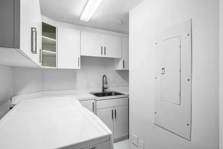 Laundry area featuring white cabinetry, integrated open shelving, a stainless steel sink with a high-arc faucet, and solid-surface countertops