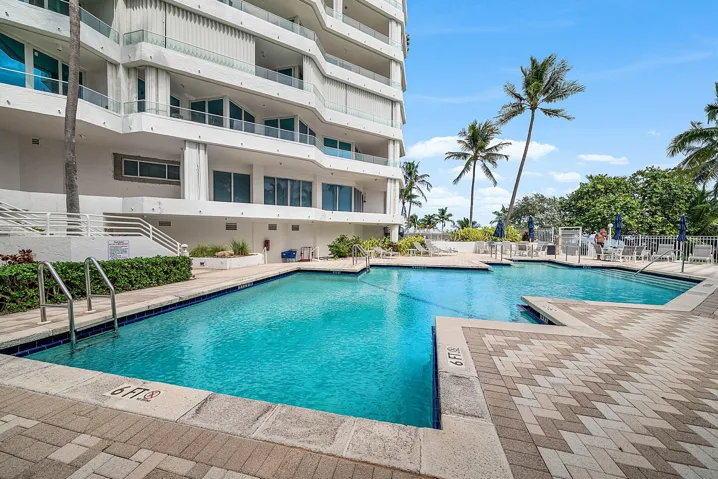 Swimming pool with paver decking, metal handrails, and surrounding mature palm trees