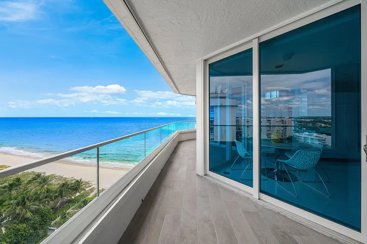 Covered terrace featuring wood-finish tile flooring, floor-to-ceiling glass sliding doors, and a glass panel railing overlooking the coastline