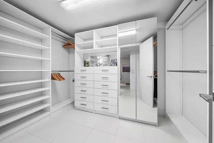 Custom storage closet featuring floor-to-ceiling white shelving, integrated multi-drawer cabinetry, full-length mirror panels, and metallic hardware