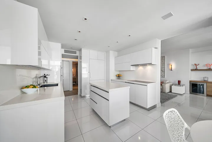 Minimalist kitchen featuring high-gloss white cabinetry, quartz countertops, a central island, recessed ceiling lighting, and polished tile flooring