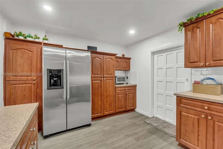 Kitchen featuring wood-finish cabinetry, stainless steel side-by-side refrigerator, speckled solid-surface countertops, recessed lighting, and multi-panel interior door