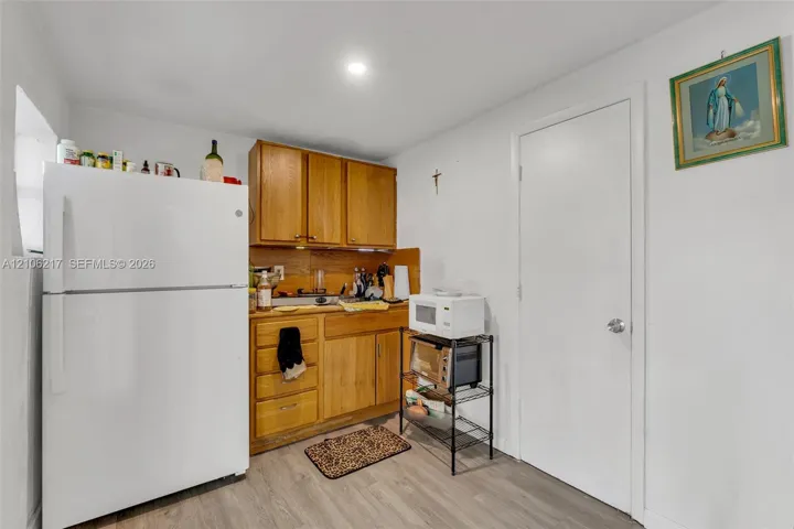 Kitchen area featuring natural-finish wood cabinetry, wood-finish flooring, a full-size white refrigerator, and a solid-panel interior door