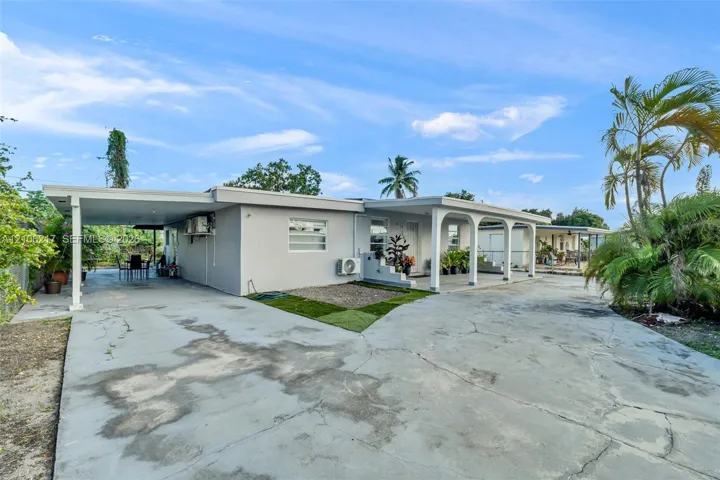 Single-story exterior featuring a covered carport, arched front porch detailing, concrete driveway, and exterior wall-mounted HVAC unit