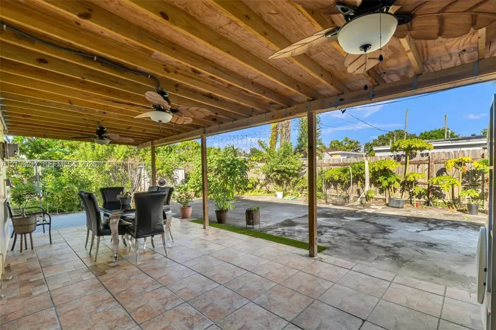 Covered patio featuring tiled flooring, an exposed wood-beam ceiling, and dual ceiling fans