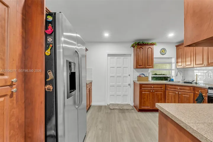 Kitchen featuring wood cabinetry, stainless steel refrigerator, stone-finish countertops, recessed lighting, and wood-finish flooring