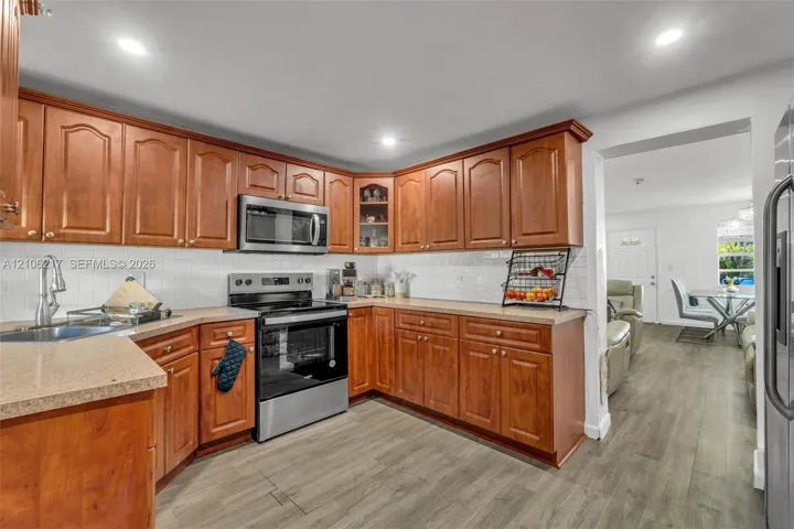 Kitchen featuring wood cabinetry, stainless steel appliances, white subway tile backsplash, solid-surface countertops, and wood-finish flooring