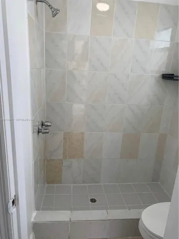 Walk-in shower enclosure featuring light-toned decorative wall tile, a square-tiled basin, and a metal shower head and handle set