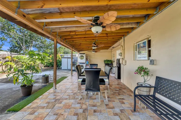 Covered patio featuring patterned tile flooring, exposed wood-beam ceiling, and multiple ceiling fans