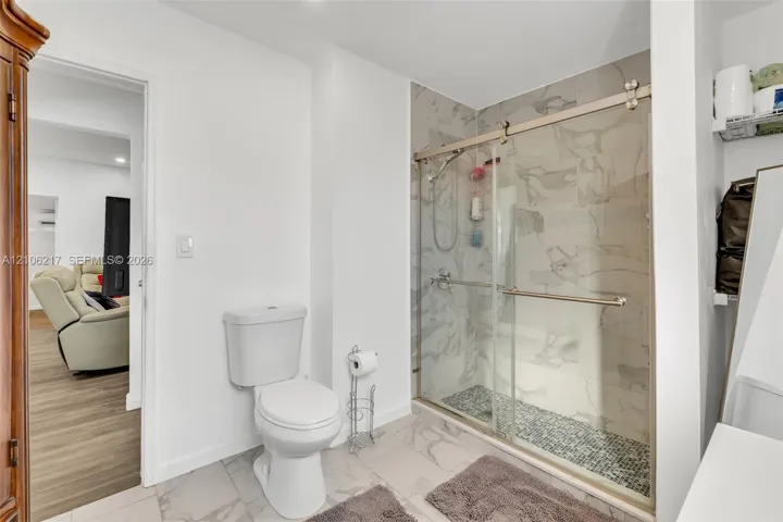 Walk-in shower featuring glass sliding doors, stone-finish wall tiling, and a textured stone-tiled shower floor