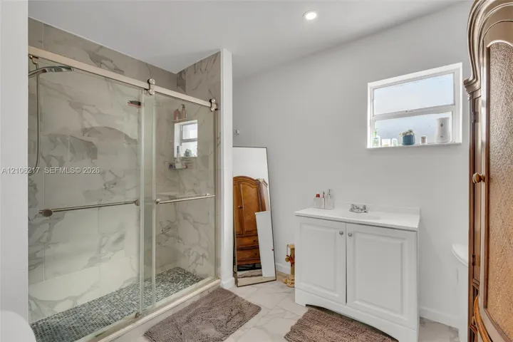 Walk-in shower with sliding glass doors, floor-to-ceiling stone-style tile surround, mosaic stone shower floor, and a white vanity cabinet with an integrated top
