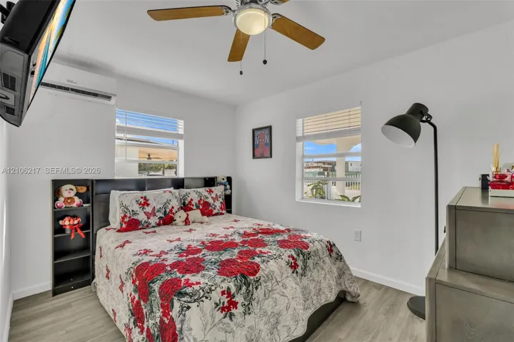 Room featuring wood-finish flooring, a wall-mounted ductless air conditioning unit, and a ceiling fan with integrated lighting