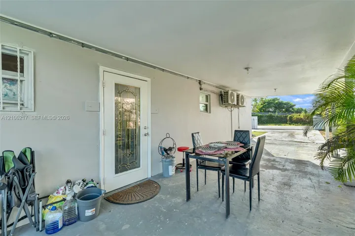 Covered concrete patio featuring a glass-panel entry door and exterior wall-mounted cooling units