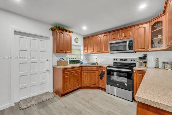 Kitchen featuring wood cabinetry, stainless steel appliances, white subway tile backsplash, solid surface countertops, and wood-finish flooring