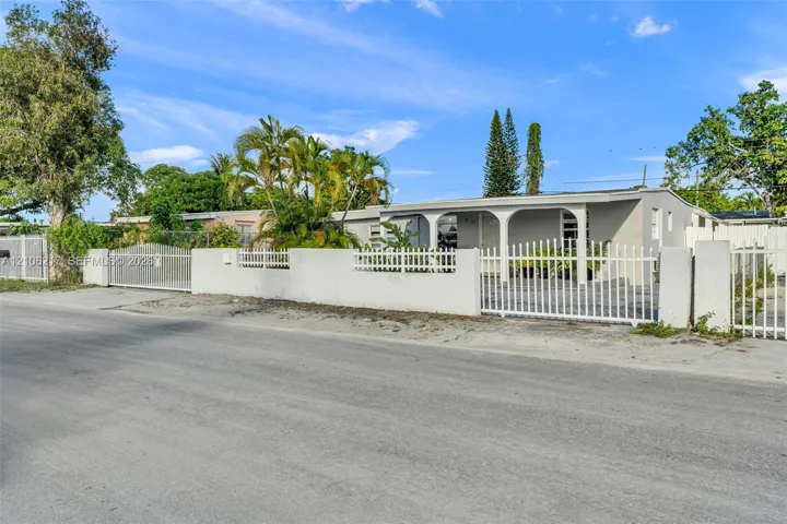 Exterior facade featuring a covered front porch with arched columns, enclosed by a perimeter wall with integrated metal fencing and gated entry