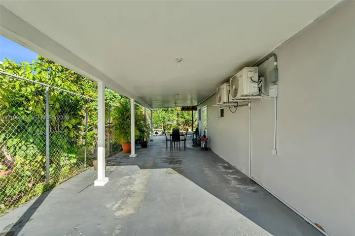 Covered outdoor patio with a concrete floor, supporting columns, and wall-mounted air conditioning units