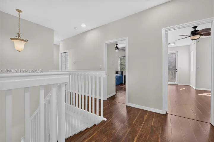 Hallway featuring wood-finish flooring, white spindle balustrades, neutral paint palette, recessed lighting, and a pendant light fixture