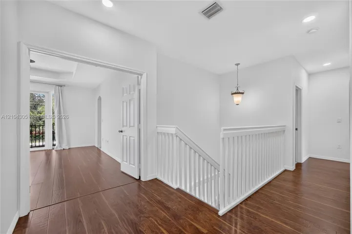 Staircase landing featuring wood-finish flooring, a white spindle railing, recessed lighting, and a traditional pendant fixture