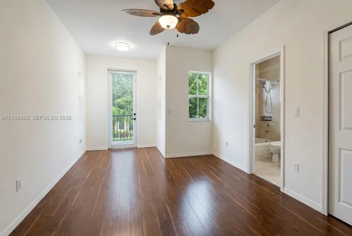 Room featuring wood-finish flooring, ceiling fan with palm-style blades, single-pane windows, glass-panel entry door, and multi-panel interior door
