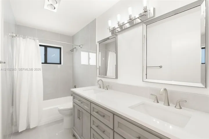 Bathroom featuring a dual-sink vanity with a solid-surface countertop, rectangular undermount basins, brushed nickel hardware, and two framed wall mirrors