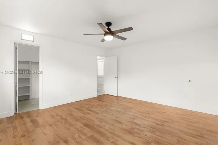 Primary bedroom Wood-finish flooring, multi-blade ceiling fan with integrated light, and walk-in closet with built-in shelving