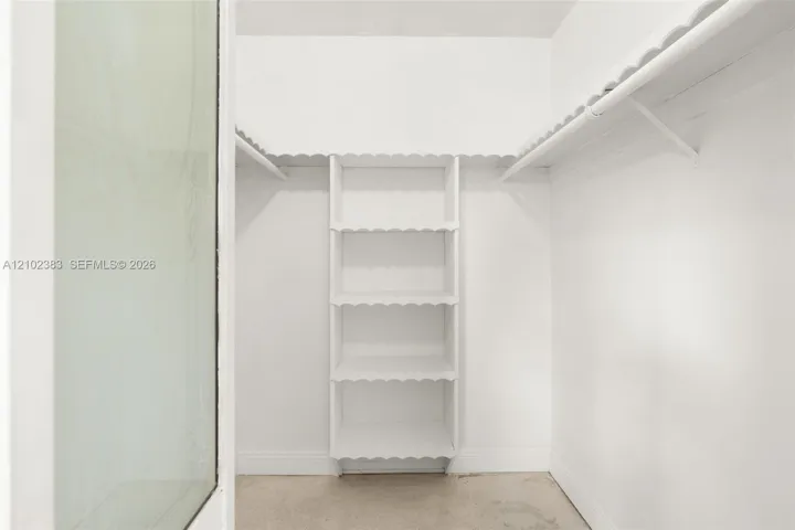 Primary walk-in closet featuring white built-in shelving, scalloped-edge wood trim, and a hanging rod