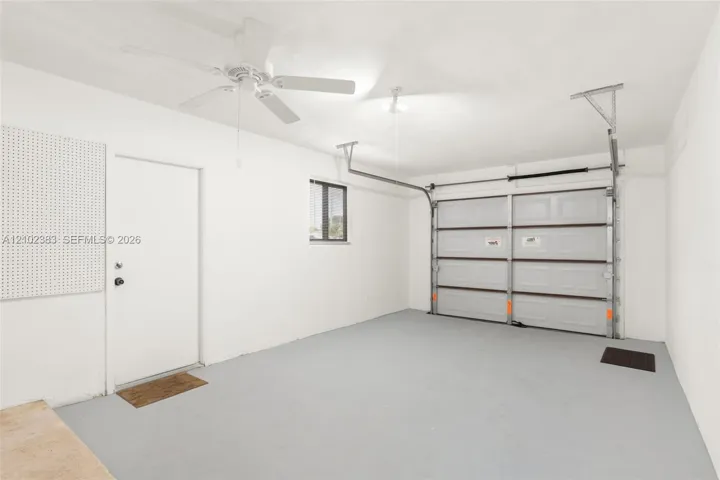 Enclosed garage featuring a multi-panel overhead door, finished concrete flooring, a ceiling-mounted fan, and integrated wall-mounted pegboard storage
