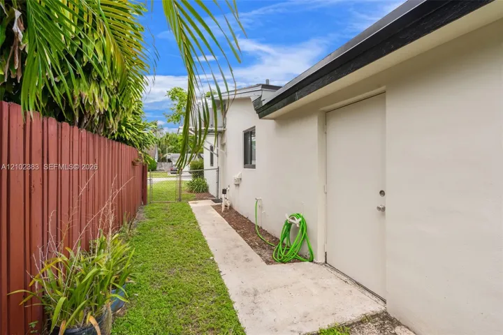 Exterior side walkway featuring a concrete path, stucco wall finish, metal fencing, and integrated outdoor lighting fixture