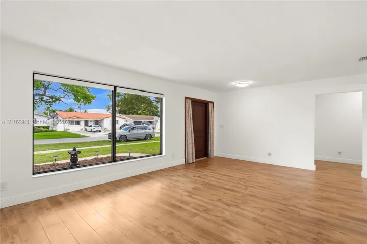 Interior space featuring wood-finish flooring, a large picture window, a solid-panel door, and a ceiling-mounted light fixture