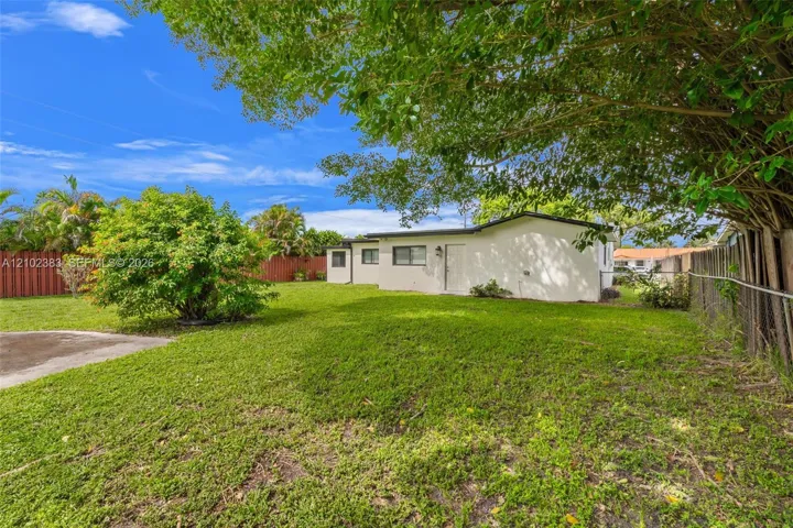 Spacious backyard featuring a manicured lawn, mature trees, concrete patio area, and privacy fencing