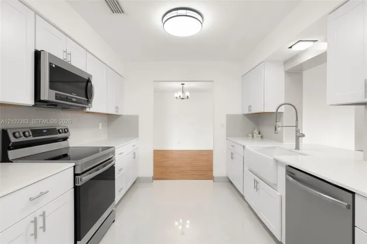 Kitchen featuring white shaker-style cabinetry, solid-surface countertops, a farmhouse-style sink with a pull-down faucet, and stainless steel appliances