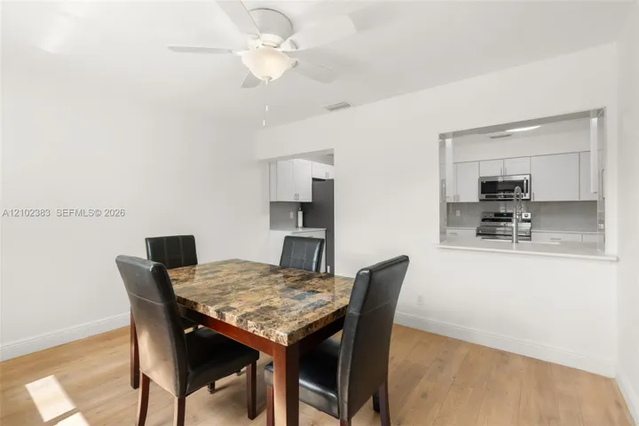 Breakfast area featuring wood-finish flooring, a ceiling fan with integrated lighting, and a kitchen passthrough with a countertop ledge