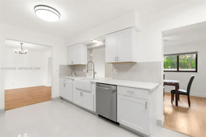 Kitchen featuring white shaker-style cabinetry, quartz countertops, a white farmhouse sink with a gooseneck faucet, stainless steel dishwasher, and polished tile flooring