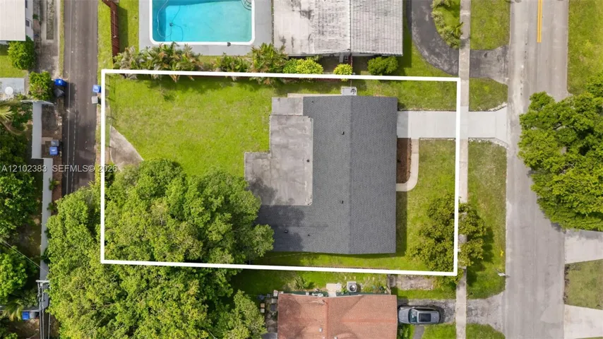 Aerial view of property featuring a rectangular lot, concrete driveway, asphalt shingle roof, and expansive lawn area