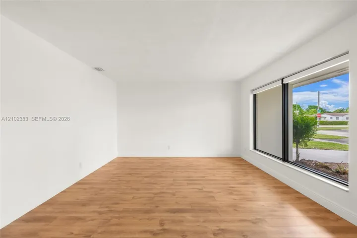 Neutral-toned interior space featuring wood-finish flooring, a expansive picture window with black frames, and recessed lighting