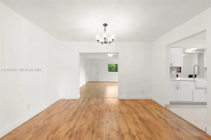 Dining area featuring wood-finish flooring, a contemporary multi-light chandelier, and white cabinetry with a farmhouse-style sink