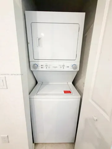 Stacked white washer and dryer unit located within a recessed closet enclosure