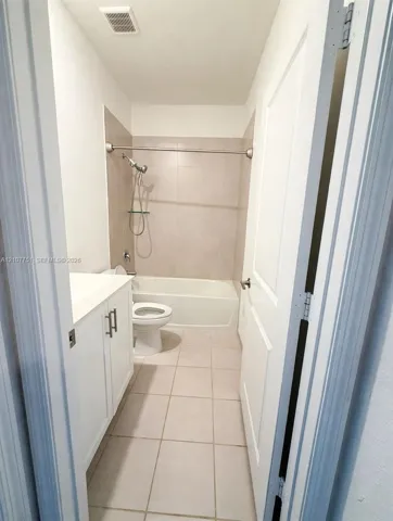 Bathroom featuring a white vanity cabinet with a solid surface countertop, ceramic tile flooring, a shower-tub combination with tiled surround, and a chrome hand-held shower fixture