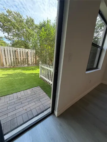Backyard featuring a paved stone patio, synthetic turf lawn, white picket fencing, and a perimeter privacy fence