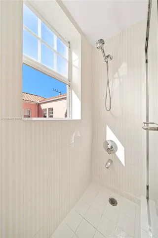Shower enclosure featuring floor-to-ceiling vertical ceramic wall tile, a hand-held shower head, chrome fixtures, and a recessed window
