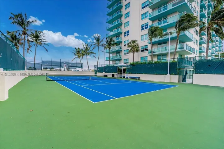 Tennis court with blue surface, perimeter fencing, and surrounding palm trees