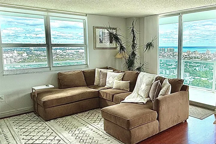 Living area featuring floor-to-ceiling windows, wood-finish flooring, and expansive panoramic cityscape and ocean scenery