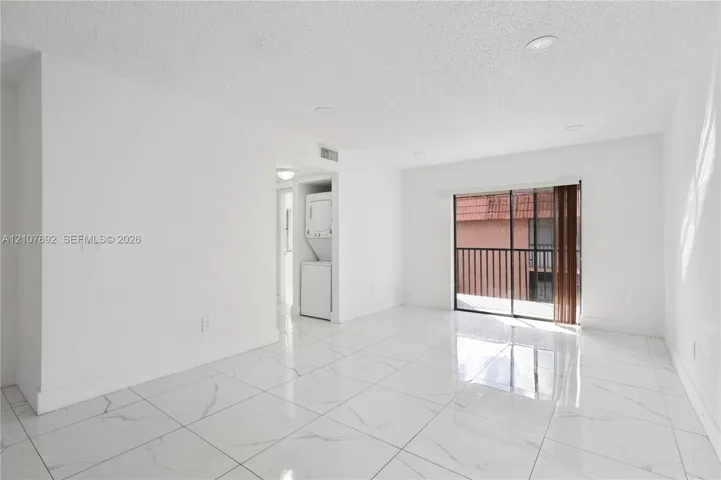 Large-format tile flooring, recessed ceiling lighting, sliding glass door with external balcony access, and stacked laundry unit