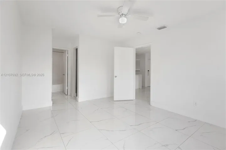Bright interior room featuring large-format tile flooring with veining, white wall finishes, and a ceiling-mounted fan with integrated light