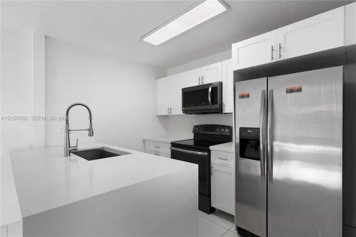 Kitchen featuring white cabinetry, quartz countertops, a stainless steel undermount sink with a pull-down sprayer faucet, and stainless steel appliances