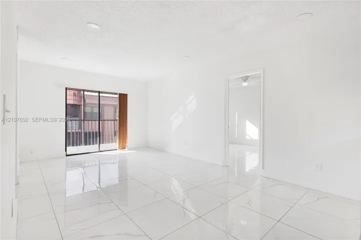 Large-format polished tile flooring, recessed ceiling lighting, sliding glass door with balcony access, and crisp white wall finishes